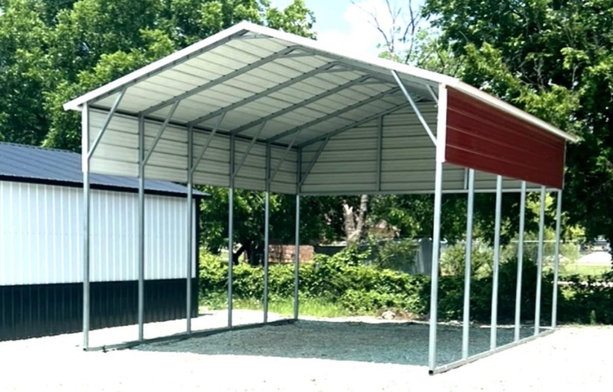 Open steel carport on a gravel pad, white gable roof on bare steel posts with a red panel closing one end