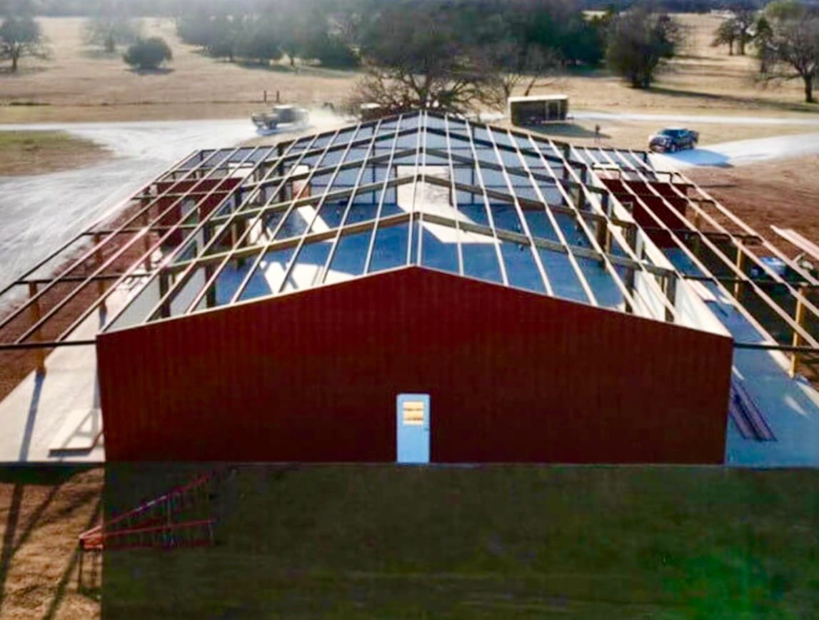 Red iron frame seen from above part way through construction, purlins and rafters in place and one end wall sheeted in red